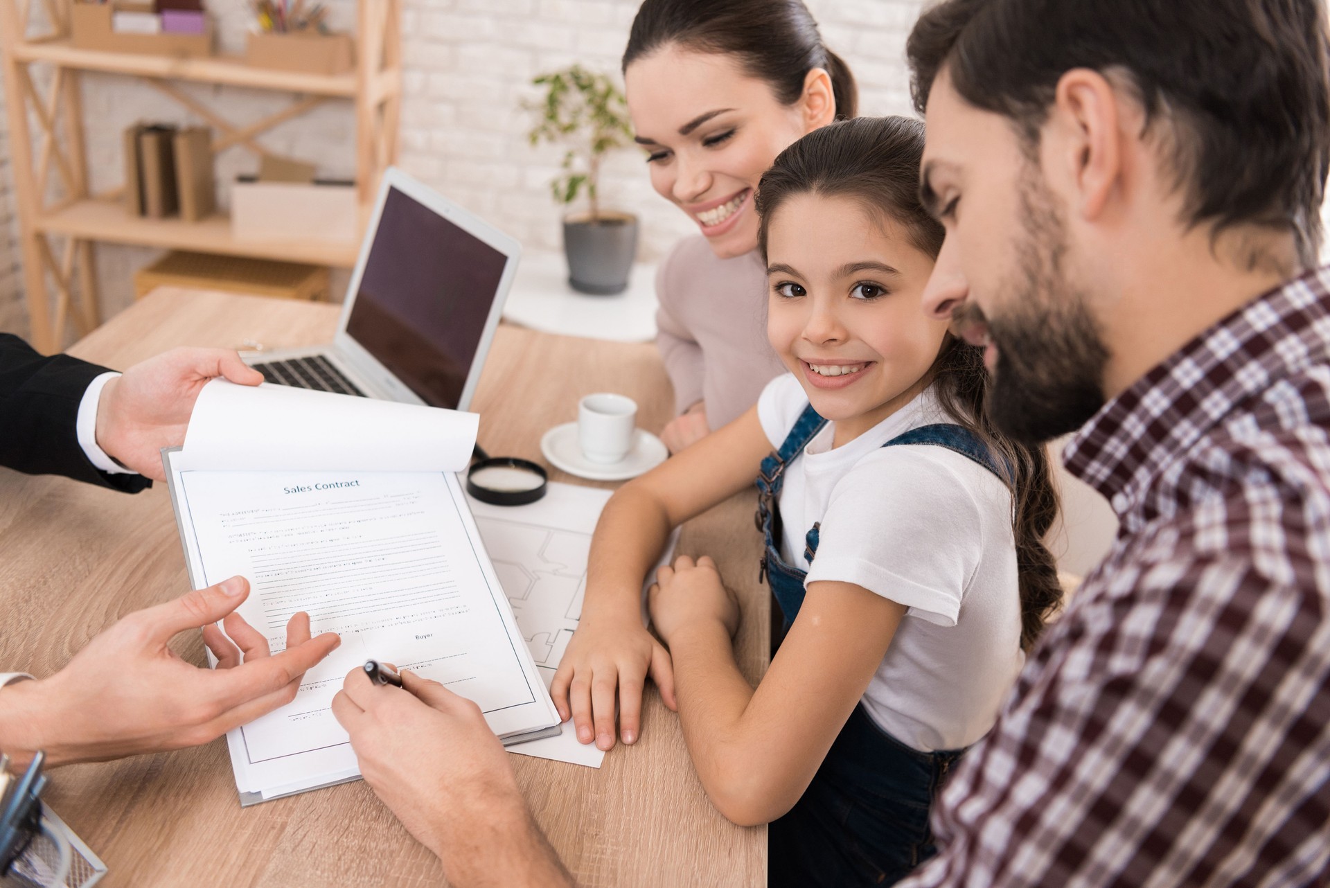 Adult father with wife and daughter signs sales contract in office of Real Estate Agent.